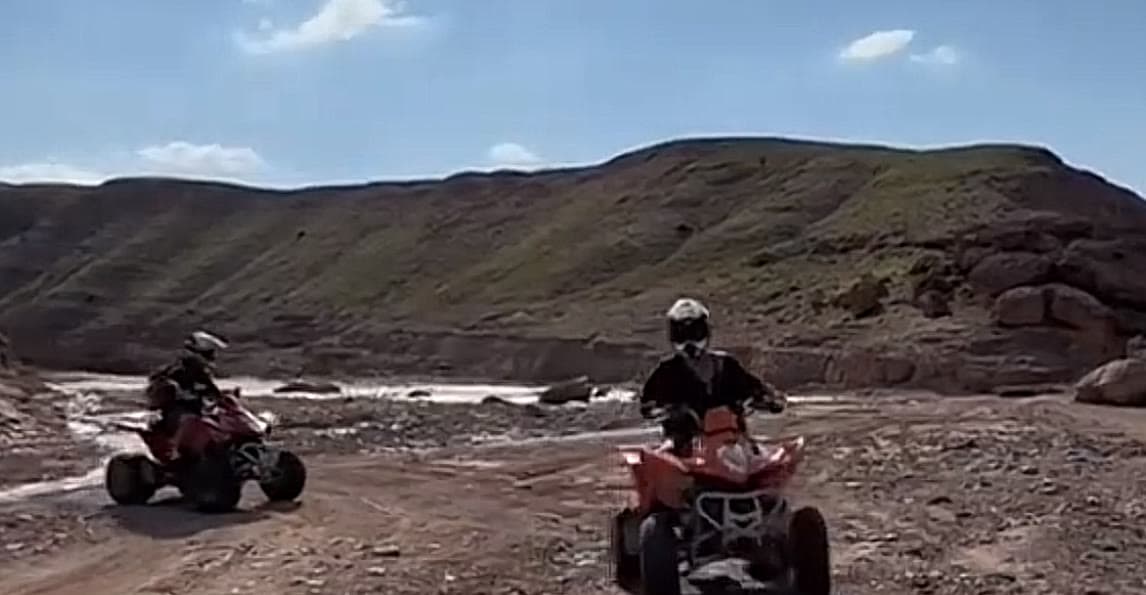 Two quad bikes riding along a rocky track below the hills of the Agafay desert.