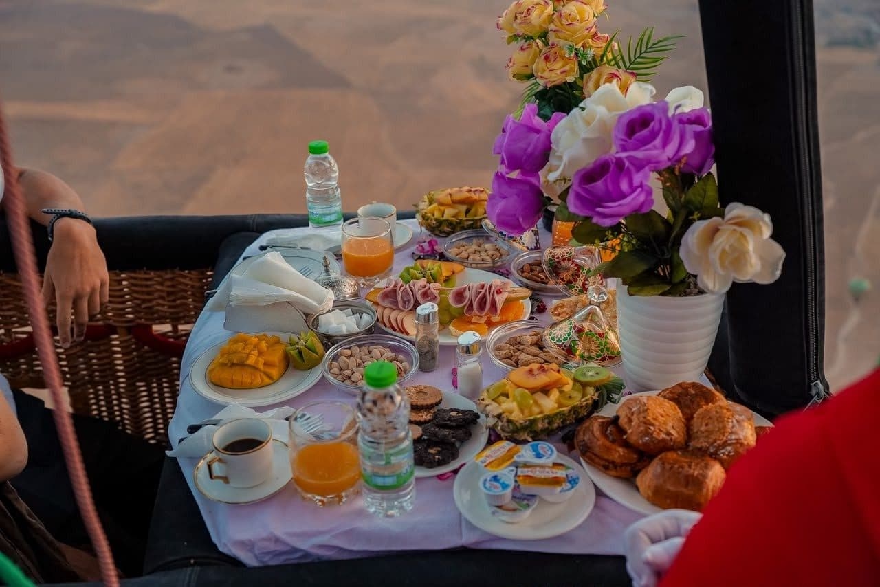 Breakfast set inside a hot air balloon basket on the ground, with the Atlas Mountains behind it.