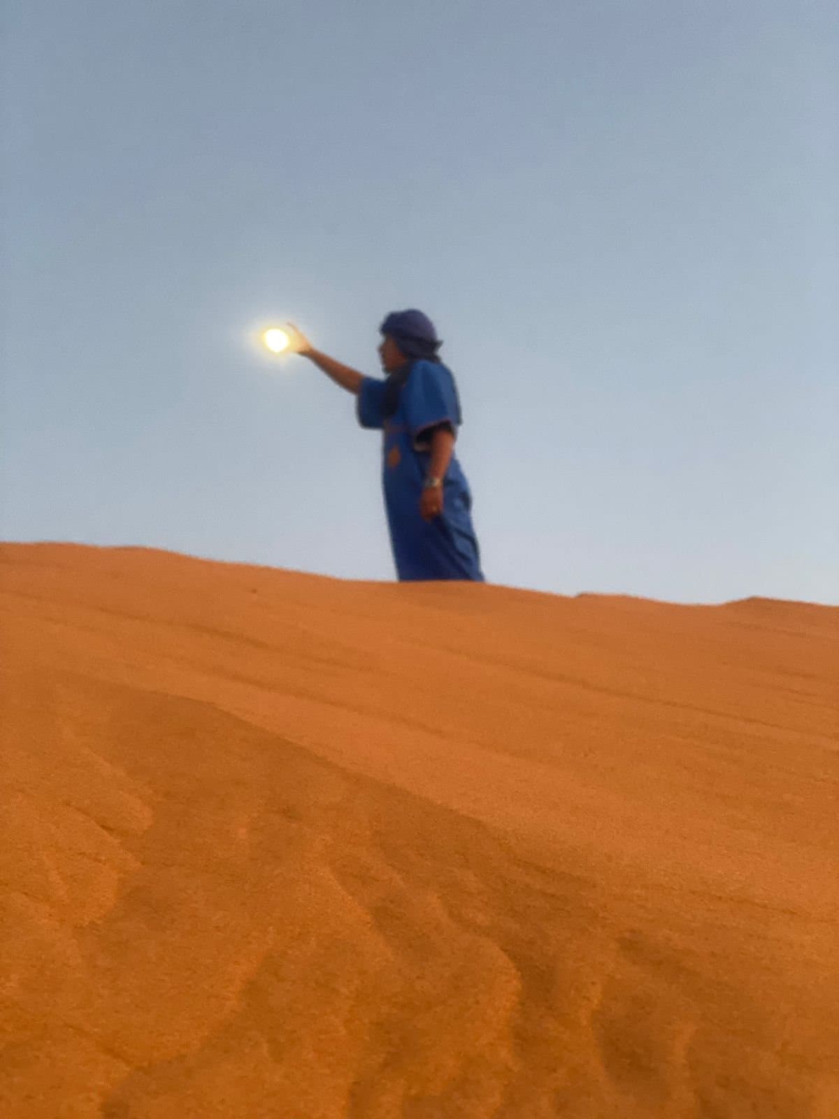 A desert guide at Merzouga framing the moon above the Erg Chebbi dunes.